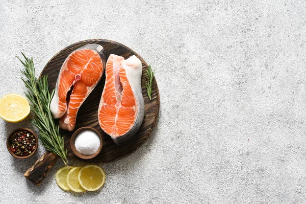 Baharatlı somon bifteği hafif beton arka planda yuvarlak ahşap bir tahtanın üzerinde pişirmeye hazır..