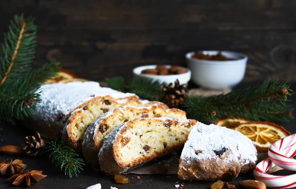 Sliced homemade Christmas dessert stollen with raisins and nuts on  rustic table with cinnamon. Christmas tree branches, selective focus