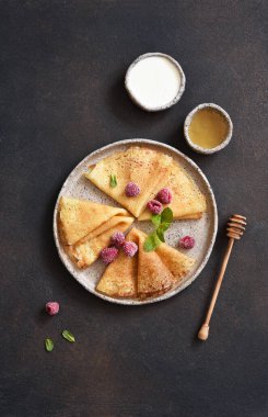 Ekşi kremalı, ballı ve böğürtlenli, ahududulu ve koyu betondan arkaplanlı ince krepler. Bir yığın krep. Yukarıdan görüntüle.