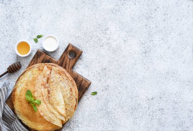 Ekşi kremalı ve ballı ince krepler beton zemin üzerinde tahta bir tahtanın üzerinde. Bir yığın krep. Yukarıdan görüntüle.