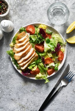 Salatayı domatesle karıştır ve tavuklu filetoyu beton arka planda bir tabağa koy..