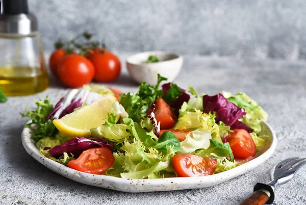 Vegetable mix salad with tomatoes and sauce on a concrete background.