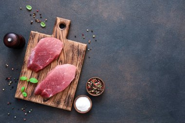 Ahşap bir tahtanın üzerinde biftek ve beton bir arka planda baharatlar..