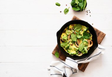 Ispanaklı ve mantarlı omlet. Hafif ahşap arka planda dökme demir bir tavada. Ispanaklı Fritata..