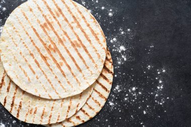 Izgara tortilla. Meksika yassı ekmeği - siyah beton bir zemin üzerinde un ile tortilla.