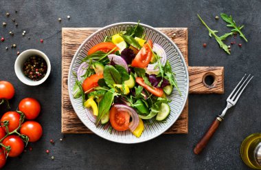 Salatayı domates, soğan ve zeytinyağıyla karıştırın. Siyah beton kaplama bir tabakta. Yukarıdan görüntüle.