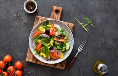 Salatayı domates, soğan ve zeytinyağıyla karıştırın. Siyah beton arka planda tahta bir tabakta. Yukarıdan görüntüle.