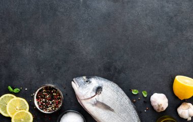 Siyah beton arka planda limon ve baharatlı çiğ dorado..