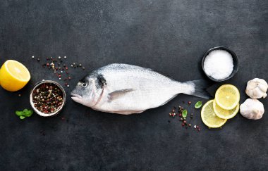 Siyah beton arka planda limon ve baharatlı çiğ dorado..