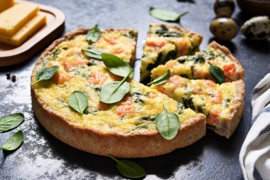 Somon ve ıspanaklı tart, siyah beton arka planda peynir. Balıklı kiş..