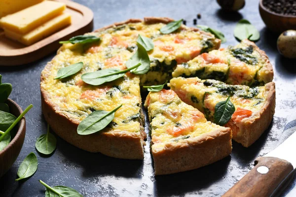 Tart with salmon and spinach, cheese on a black concrete background. Quiche with fish.