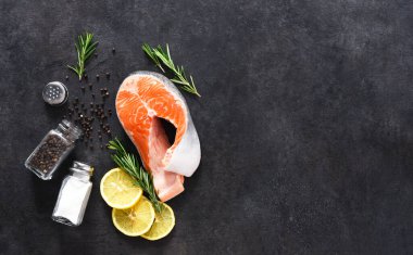 Beton bir arka planda çiğ somon bifteği, tuz ve biberiye. Balık pişirmek için gerekli malzemeler.