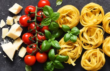 Tagliatele makarna, domates, fesleğen ve parmesan peyniri siyah beton arka planda. Makarna malzemeleri ve metin alanı. Düzen.