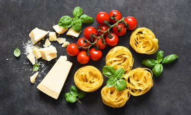 Tagliatele makarna, domates, fesleğen ve parmesan peyniri siyah beton arka planda. Makarna malzemeleri ve metin alanı. Düzen.