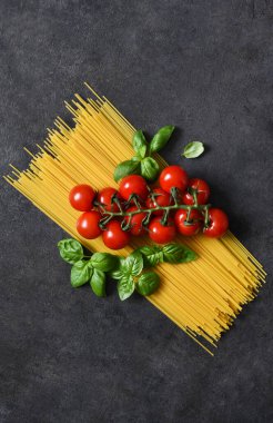Siyah beton arka planda spagetti, domates ve fesleğen. Makarna malzemeleri ve metin alanı. Düzen.