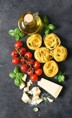 Tagliatele makarna, domates, fesleğen ve parmesan peyniri siyah beton arka planda. Makarna malzemeleri ve metin alanı. Düzen.