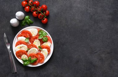 Caprese bir domates ve mozzarella aperatifi. Siyah arka planda yazılı geleneksel İtalyan salatası. Yukarıdan görüntüle.