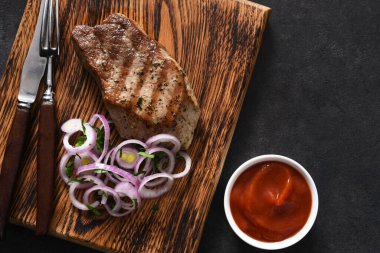 Ahşap bir tahtada ızgara biftek, soğan ve domates sosu. Kızarmış et..