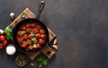 Köfteler, domates soslu, sarımsaklı ve fesleğenli kahverengi arka planda kızartma tavasında..