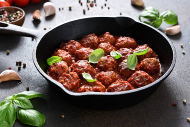 Köfteler, domates soslu, sarımsaklı ve fesleğenli kahverengi arka planda kızartma tavasında..