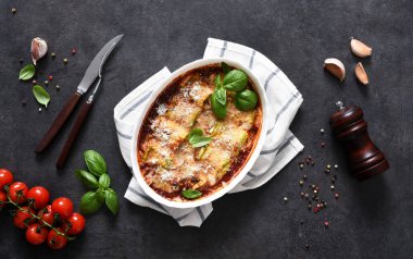 Pişmiş kabak dürümleri, ricotta peyniri, domates sosu ve siyah arka planda parmesan..