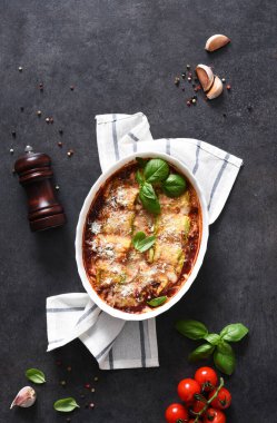 Pişmiş kabak dürümleri, ricotta peyniri, domates sosu ve siyah arka planda parmesan..