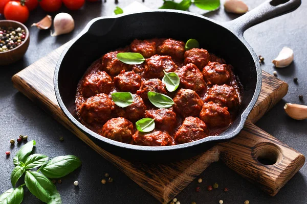 Meat balls with tomato sauce with garlic and basil in a frying pan on a brown background.