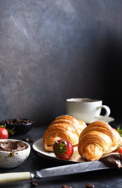 Çikolatalı kruvasan ve bir fincan kahve, mutfak masasında çilek.. 