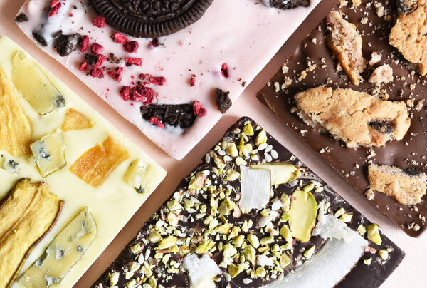Handmade chocolate with different fillings: cookies, lavender, rose, orange, pear, coconut, walnut, candied fruit, cheese on a delicate beige background.