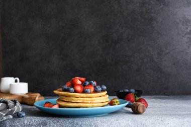 Mavi bir tabakta ev yapımı krepler. Beton bir arka planda böğürtlen ve şurup var..