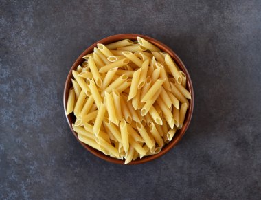 Karanlık bir arka plan üzerine bir kase içinde pişmemiş makarna