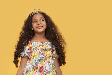 Koyu tenli, uzun kıvırcık saçlı, sarı arka planda renkli elbiseler giyen genç bir kızın yarım boy portresi.