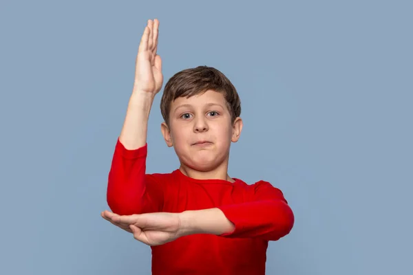 スタジオショットの自信に満ちた若い男の子の赤いシャツを身に着けている彼の手を引っ張っ質問に答えるために青の背景 — ストック写真