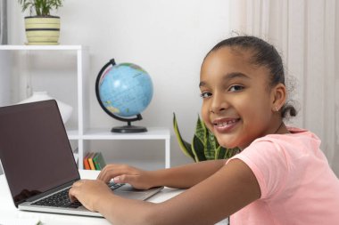 Öğrenci kız içeride masada oturuyor ve ev ödevini bir dizüstü bilgisayar ve internet kullanarak yapıyor ya da internetten veya karantina sırasında uzaktan bağlanıyor.