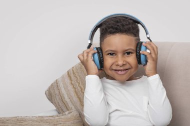 Koyu tenli, mavi kulaklıklı, kanepede oturmuş müzik dinleyen Afrikalı bir çocuğun portresini kapat.