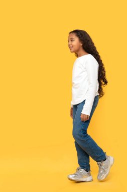 Beyaz gömlek ve kot pantolon giyen kıvırcık saçlı, koyu tenli Afrikalı genç kızın tam boy portresi sarı arka planda duruyor..