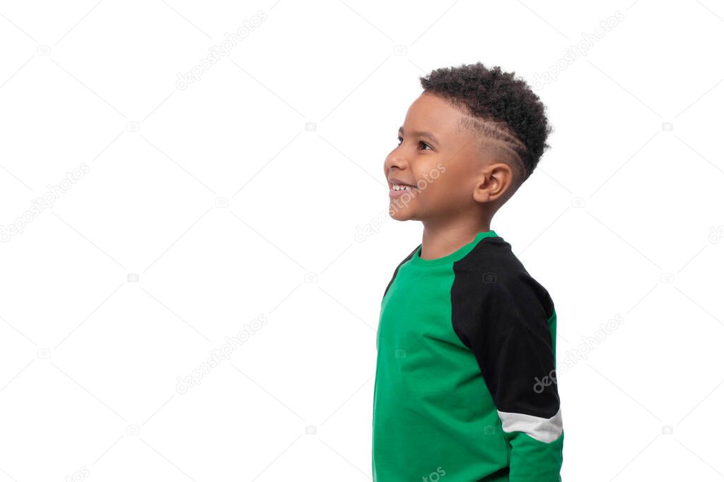 Waist up emotional profile portrait of little dark skinned African   boy wearing green shirt against white background in studio