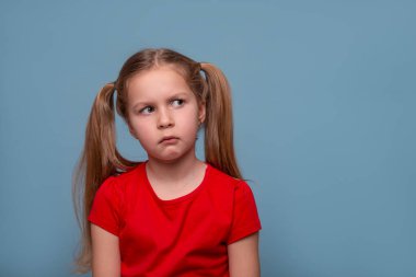 Çanta dudaklı ve yaralı küçük bir kızın yakın plan portresi. Kırmızı gömlekli, mavi arka planda fotokopi alanı olan bir kız. Çocuk duyguları, yüz ifadesi kavramı.  