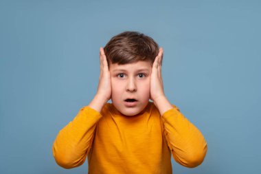 Stres, şok, korkunç. Sarı tişörtlü genç bir çocuğun duygusal yakın plan portresi. Kafasını mavi arka plana yapıştırıp fotokopi çekiyor. Çocuk duyguları, yüz ifadesi kavramı.  