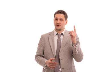 Bej takım elbiseli, kravatlı genç bir adamın yarım boy portresi işaret parmağını beyaz arka plana doğru kaldırarak bir şeyi kanıtlıyor.. 