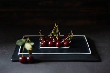 Siyah arkaplana karşı siyah bir plaka üzerinde duran kiraz kareleri..  