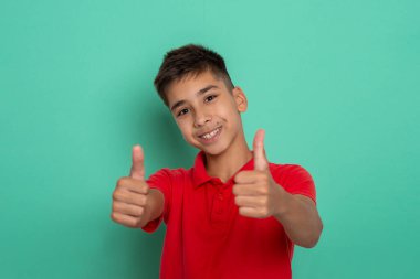 Kırmızı tişörtlü, yeşil arka planda, iki elini de işaret eden gülümseyen bir gencin stüdyo fotoğrafı..