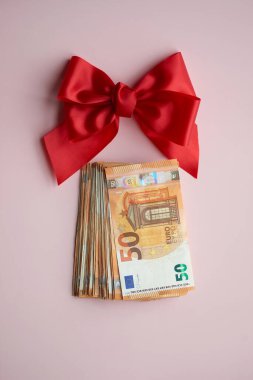 50 avroluk banknotlar kırmızı saten bir kurdelenin altına yerleştirilmiş. Pembe bir arka plana karşılık hediye, bonus, nakit ödül olarak.