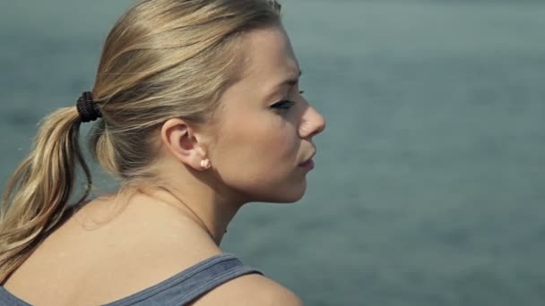 Close up girl sitting by the water and looking into the distance — Stock Video