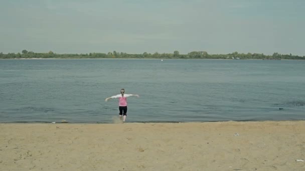 Dívka, radostně běží v blízkosti vody na špinavé pláži — Stock video
