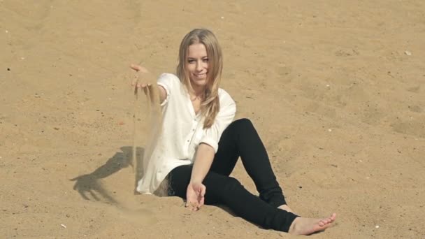 Beautiful girl sitting on the beach and looking at the camera — Stock Video