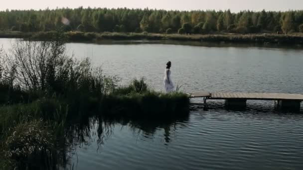 Hermosa morena en un vestido blanco camina por el puente — Vídeos de Stock