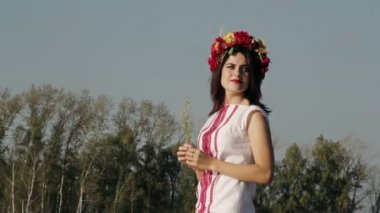 Güneşin sıcaklığına zevk kafasında bir çelenk ile Rus ulusal elbiseli güzel kız