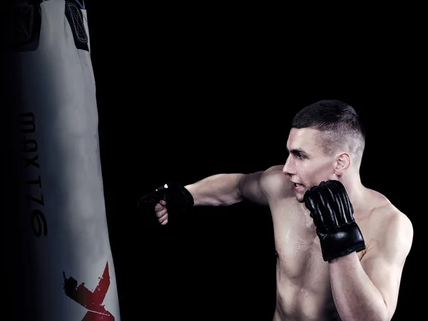 Young man hits punching bag on black background — Stock Photo, Image