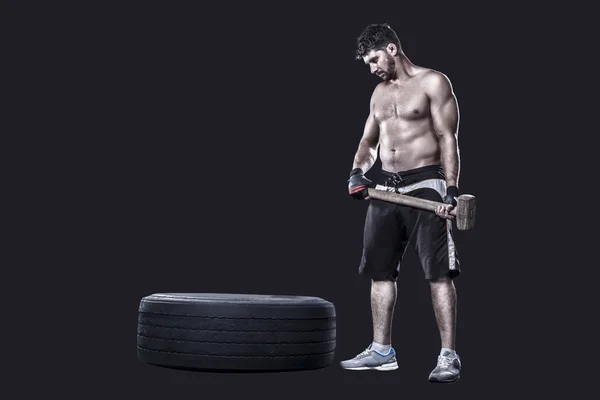 Sportsman avec un marteau à côté de pneu isolé sur noir — Photo